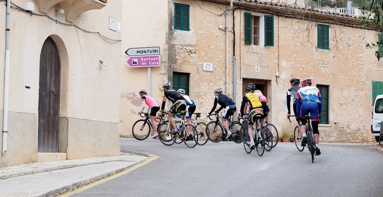 Group of cyclists turning a corner on a street with signs for Montuïri and Santuari de Cura.